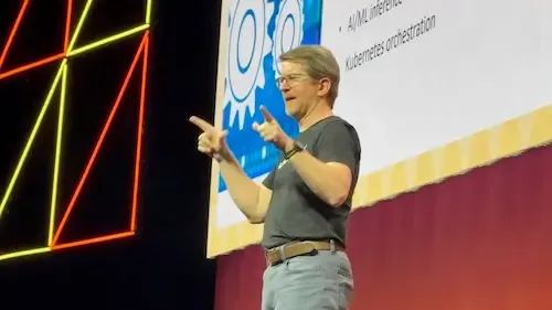 a man standing on the stage presenting the talk