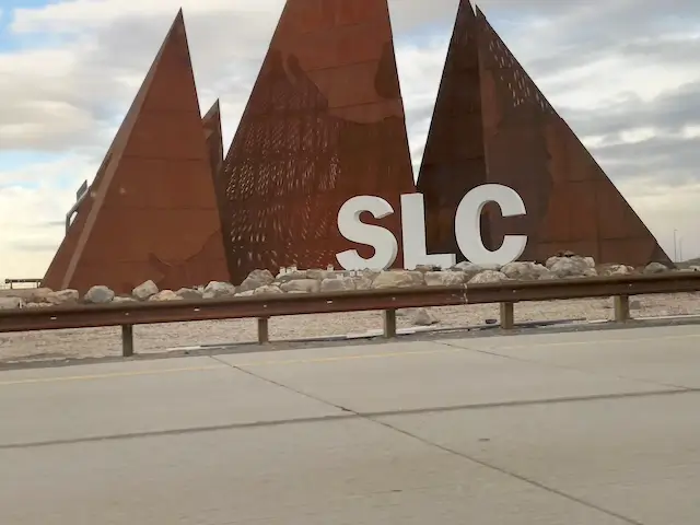 A rust-colored metal sculpture resembling mountain peaks spelling SLC